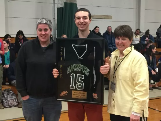 A young man posed with his retired jersey and two women on either side of him, in front of spectators on the bleachers.
