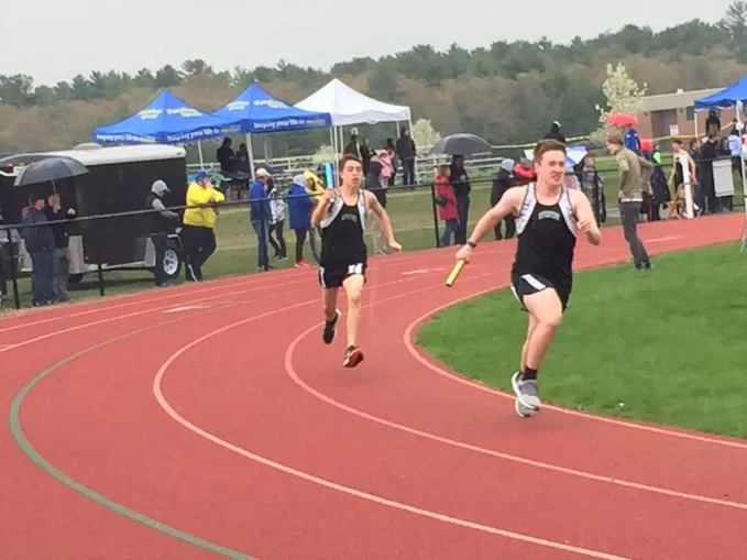 Two boys competing in a relay race on a cloudy day.