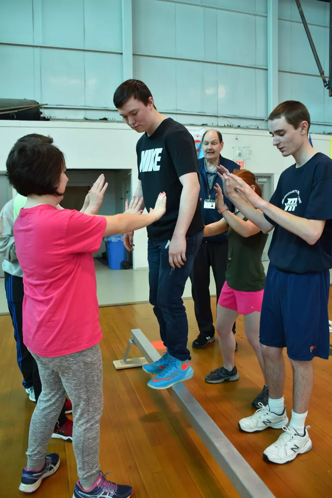 Several people helping a student remain balanced on a balance beam.
